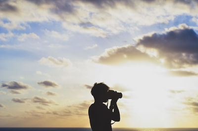Silhouette woman photographing against sky during sunset