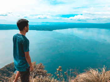 Rear view of man standing by sea against the sky while hiking in the mountain