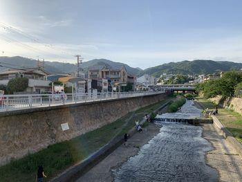 Bridge over river by buildings in city against sky