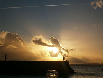 Silhouette people on jetty over sea during sunset