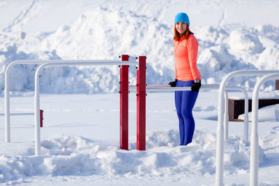 A young woman in bright sportswear makes pull-ups on horizontal bars on a bright winter day