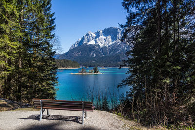 Bench by lake against blue sky