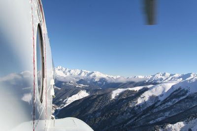 Cropped image of airplane flying over snowcapped mountains against blue sky