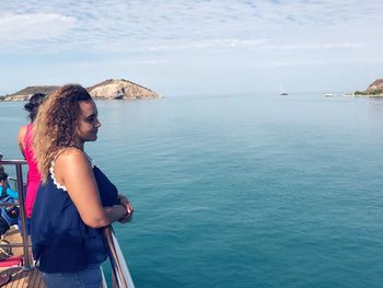 Woman looking away while standing on boat in sea against sky