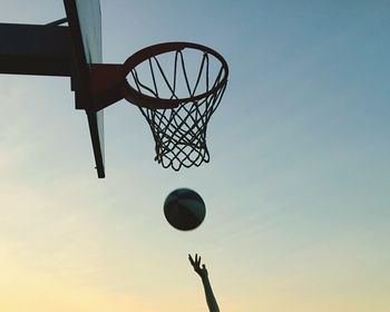 Cropped hands playing basketball against clear sky during sunset