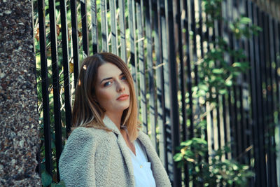 Portrait of young woman standing by fence at park