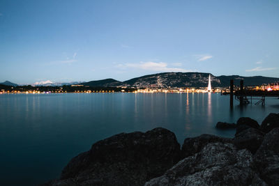 Illuminated city by sea against sky