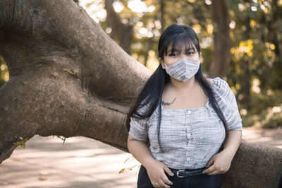 Portrait of a young woman standing against tree