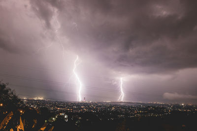 Lightning over illuminated cityscape against dramatic sky