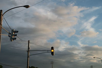Low angle view of street lights and road signals against cloudy sky