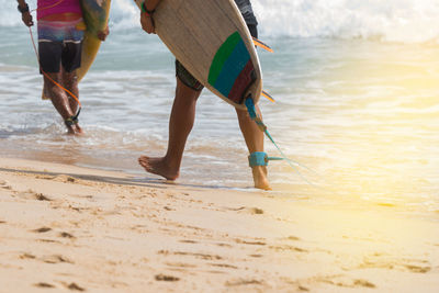 Low section of men with surfboard walking at beach