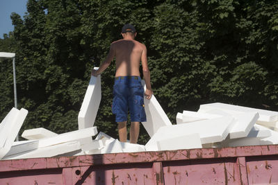 Full length of shirtless man standing against trees