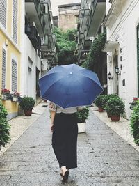 Woman holding umbrella standing on footpath amidst buildings