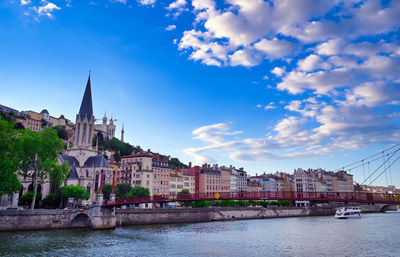 Bridge over river by buildings against sky