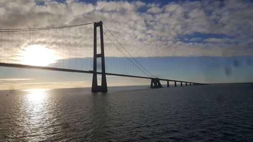 Suspension bridge over sea against sky during sunset