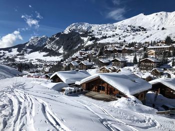 Snow covered houses against mountain backdrop and sky