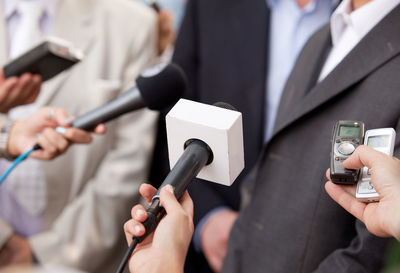 Close-up of journalists holding microphone by men