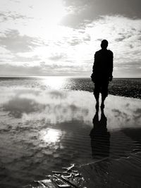 Rear view of silhouette man standing at beach against sky