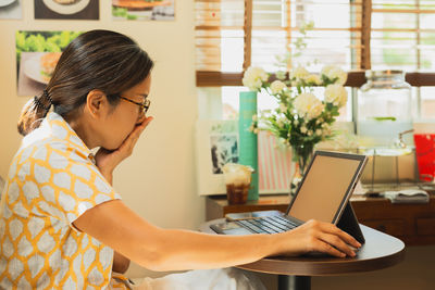 Side view of young woman using mobile phone while sitting in cafe