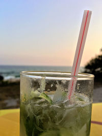 Close-up of drink in glass against sea during sunset