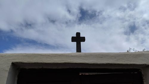 Low angle view of cross in cemetery against building