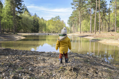 Rear view of boy standing by lake in forest