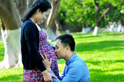 Man kissing pregnant wife belly on field