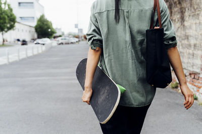 Young woman with skateboard walking on road