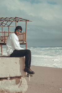 Man sitting on shore at beach against sky