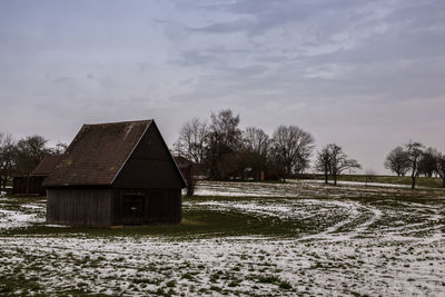 House on field by trees against sky