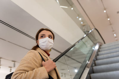 Low angle view of woman wearing mask sanding on escalator at shopping mall