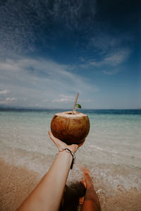 Cropped hand of woman holding coconut at beach