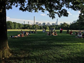 People relaxing on field in park against sky