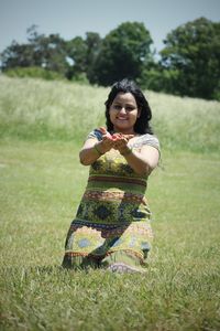 Portrait of woman holding flowers with cupped hands kneeling on grassy field
