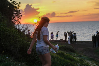 Rear view of couple standing on field against sky during sunset