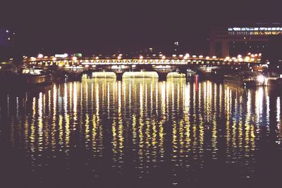 Illuminated city by river against sky at night