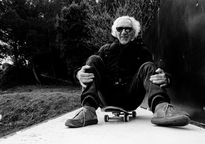 Portrait of man sitting on skateboard against plants