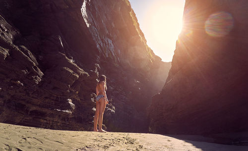 Rear view of woman wearing bikini standing amist rock formation against sky