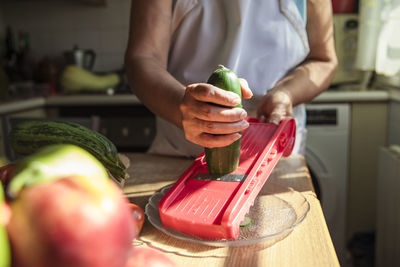 Woman slicing cucumber while making salad at kitchen