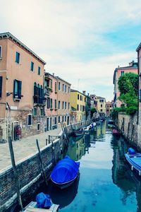 Boats moored in canal amidst buildings in city against sky