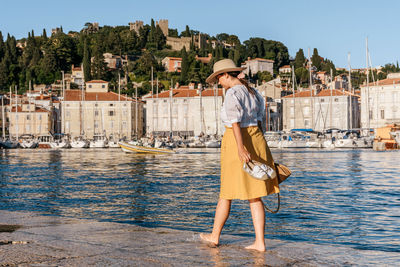 Rear view of woman walking in marina with sailing boats moored in idyllic seaside town