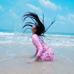 Full length of girl splashing water in sea against sky