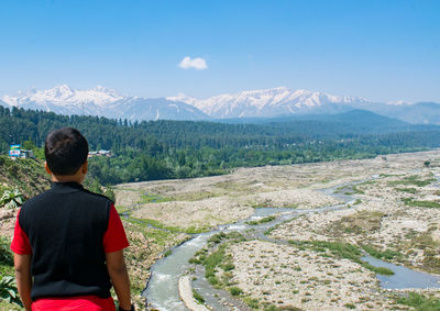 Rear view of man standing on mountain against sky