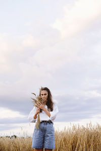 Woman walking on wheat golden field holding heap of rye. fashionable female touching wheatear