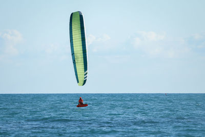 Person paragliding in sea against sky.