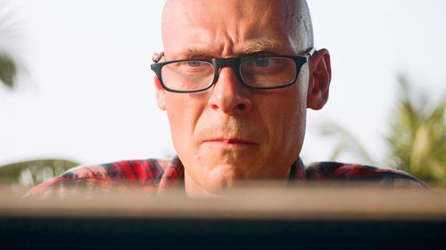 Man using laptop against trees and sky