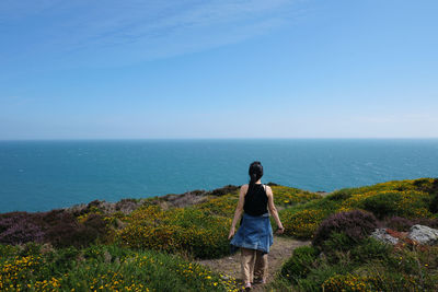 Rear view of woman walking on cliff by sea against sky