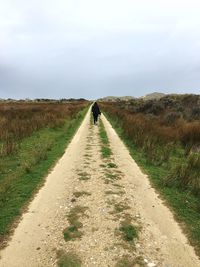 Rear view of woman walking on road amidst landscape against sky