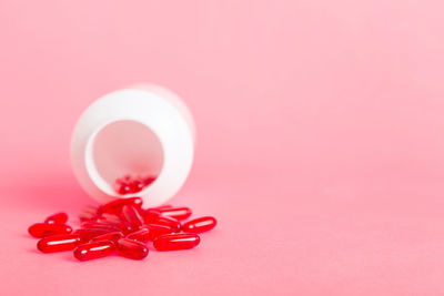 Close-up of pills spilling from bottle against pink background