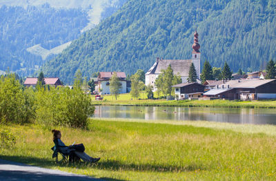 Woman sitting on grassy field against houses